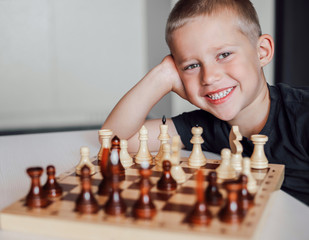 Joyfull little white boy plays chess in the room and smiles