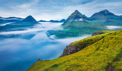 Naklejka na ściany i meble Dramatic morning view of Faroe Islands with low clouds, Denmark, Europe with low clouds. Adorable summer scene of Eysturoy island, Funningur village location. Beauty of nature concept background.