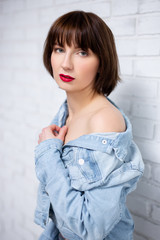portrait of young sexy woman with red lips in jeans shirt posing over white brick wall