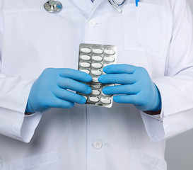 doctor therapist is dressed in a white uniform coat and blue sterile gloves is standing and holding a stack of pills in blister packs