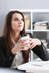 Businesswoman at workplace in office portrait during break drinks coffee from white cup smiling and looking at camera creates visibility of work and success causes trust