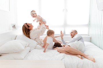 Fototapeta premium A young happy family with young children lying around, hugging, laughing on the bed at house