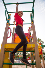Fototapeta premium Cute happy teenage girl playing on a playground, hanging walk along the monkey bars 