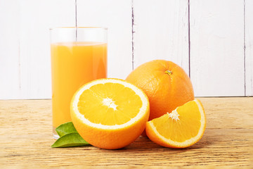 Glass of fresh orange juice with fruits cut in half and sliced with green leaf on wood background