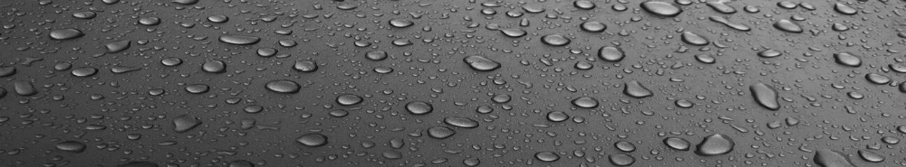 Drops of water on a black long metal surface, beautiful background after rain