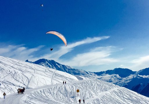 Person Flying Over Snowcapped Mountain Against Blue Sky