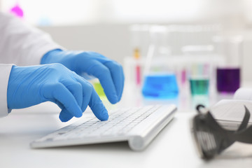 Employee chemical laboratory teacher chemist knocks his fingers keyboard makes notes electronic journal records the analysis data from reactions examining test tubes with the substance arm in gloves