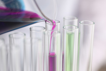 A male chemist holds test tube of glass in his hand overflows a liquid solution of potassium permanganate conducts an analysis reaction takes various versions of reagents using chemical manufacturing