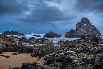 Long Exposure of rocks at the beach of the Camel Rock bay in New South Wales, Australia at a cloudy and windy day in summer with strong waves in the ocean. 