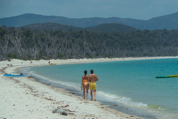 Couple on honeymoon on beach, walking on white sand, with aqua turquoise ocean. Travel, holiday, vacation, romantic, paradise, exotic. Whitsundays Islands, Queenstown, Australia.