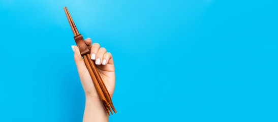 Crop image of female hand holding chopsticks on blue background. Japanese food concept with copy space