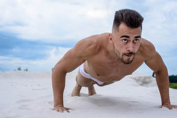 Obraz premium sexy man in white shorts is pressed from the floor in the fresh air, against white sand and blue sky.