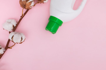 Liquid washing detergent in plastic bottle and cotton flowers on pink background.
