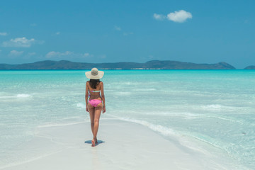Fototapeta na wymiar Woman on paradise blue beach. Tourist on Whitsundays beach, white sand, in pink bikini & hat, with aqua turquoise ocean. Travel, holiday, vacation, paradise, exotic. Whitsundays Islands, Australia.