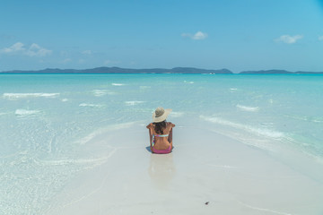 Woman on paradise blue beach. Tourist on Whitsundays beach, white sand, in pink bikini & hat, with aqua turquoise ocean. Travel, holiday, vacation, paradise, exotic. Whitsundays Islands, Australia.