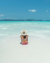 Woman on paradise blue beach. Tourist on Whitsundays beach, white sand, in pink bikini & hat, with aqua turquoise ocean. Travel, holiday, vacation, paradise, exotic. Whitsundays Islands, Australia.