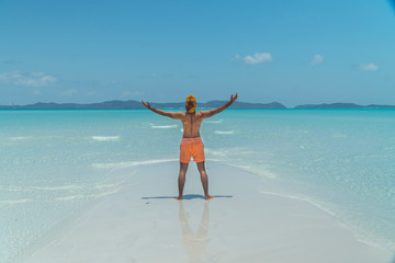 Man on paradise blue beach. Tourist on Whitsundays beach, white sand, in orange shorts, hat with aqua turquoise ocean. Travel, beauty, holiday, vacation, exotic. Whitsundays Islands, Australia.