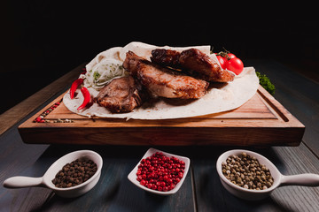 Appetizing fried meat lies on a wooden tray, among the seasonings. Studio photography of food in the cooking industry, dark background