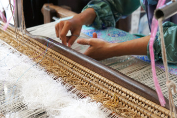 A woman is using traditional weaving machines to weave songket. Songket is a Malay traditional clothes with high quality and value.