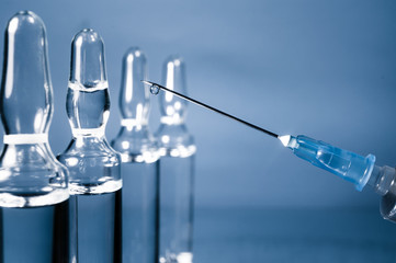 Transparent glass medical ampoule for vaccination with liquid and disposable syringe on a bluebackground . Coronavirus vaccine