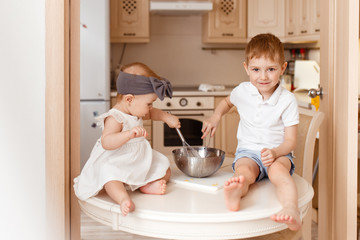 little brother and sister sit on the kitchen table and prepare Breakfast, have fun laugh play in the kitchen at home, baby, boy, girl, family, game