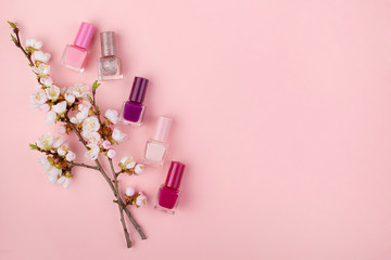 Set of nail polishes and flowers on a pink background. Beauty concept, flat lay with space for text.