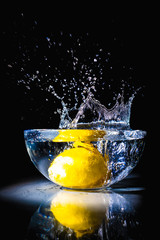 Water splash from a lemon falling into a bowl with water on black background and reflection