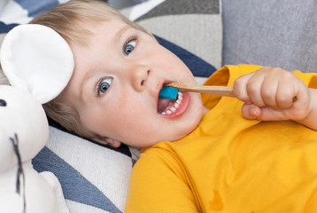 Little blond boy brushes his teeth with a wooden brush