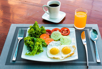 Healthy American breakfast serving with two fried eggs, fresh salad , cup of coffee and a glass of orange juice on wooden table