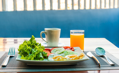 American breakfast with two fried eggs and green salad and cup of coffee , one fresh orange juice with blurred background