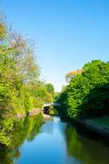Fototapeta na wymiar Landschaftsaufnahme mit einer Brücke im Hintergrund und einem Fluss im Mittelpunkt, daneben Wälder und Bäume im saftigen Grün