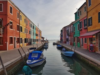 Fototapeta na wymiar Stock photo of with Burano (Venice) coloured houses and boats parked in front of them with copy space available.