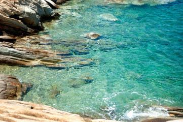Crystal clear blue sea waters at the coast on the beautiful Greek holiday island of Ios.  The rocks give way to pebbles as the Aegean sea laps the shore.