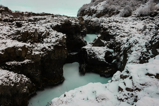 Turquoise blue water flows through a snow covered rocky canyon. Baranfossar, Iceland - legend states that its name is taken from two children who fell into the waterfall.
