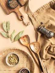 Kitchen flat lay of beige apron, small bowls with spices, metal spice mill, wood kitchen utensils on beige background. Top view. copy space