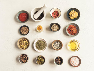 Various dry spices and sauces on a light background. Flat lay of small bowls with dijon mustard, olive oil, ketchup, capers and spices. Top view