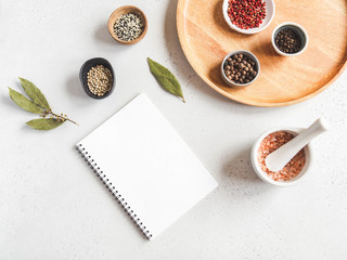 Kitchen notepad mock up for culinary text and various spices in bowl and sea salt in white mortar on white background.