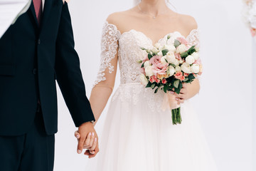 Wedding bouquet in the hands of the bride with white pink yellow roses and greenery on a beige background