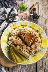 Stewed pork neck in gravy served with barley on wooden table.