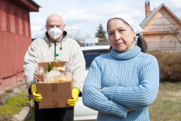 elderly male volunteer delivers food to  mature woman