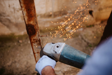 A young caucasian man with a grinder in his hand works in the yard