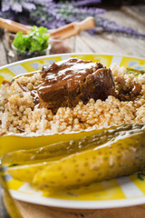 Stewed pork neck in gravy served with barley on wooden table.