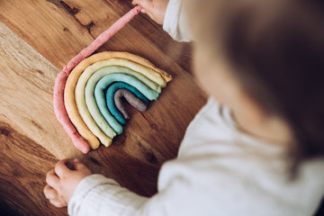 Kleinkind knetet bunten Regenbogen auf Holztisch