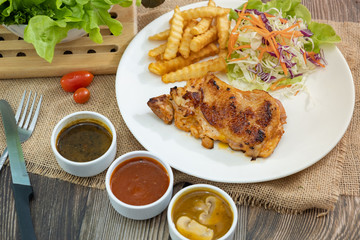 Plate of grilled chicken with french fries and vegetables bbq sauce, mushroom sauce and black pepper sauce on wooden table. 