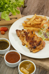 Plate of grilled chicken with french fries and vegetables bbq sauce, mushroom sauce and black pepper sauce on wooden table. 