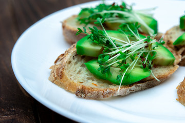 sandwiches with avocado and microgreens on a white plate. close-up. young sprouts of cressalate. healthy diet. vegetarianism. Rye bread.