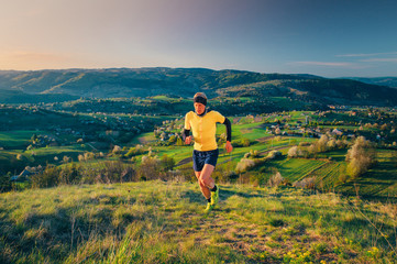 Naklejka premium Male runner training in spring morning nature. Man running up hill. Beautiful spring scenery in background. Hrinova village in Slovakia