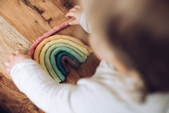 Kleinkind knetet bunten Regenbogen auf Holztisch