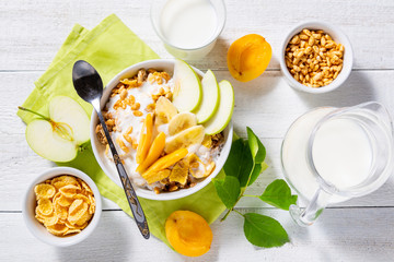 Granola and vegetarian yogurt with slices of apple, apricot, banana and a jug of milk on a white wooden background. Healthy breakfast concept. Top view