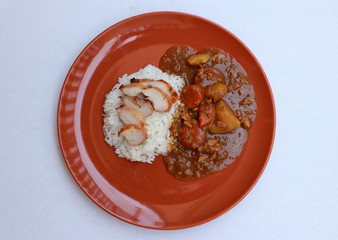 Top view, Yellow Curry Chicken with cooked rice in the round orange color of dish on white floor.